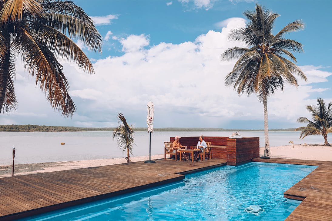 a couple relax by the pool at Tiwi Island Retreat, surrounded by white sand and palm trees